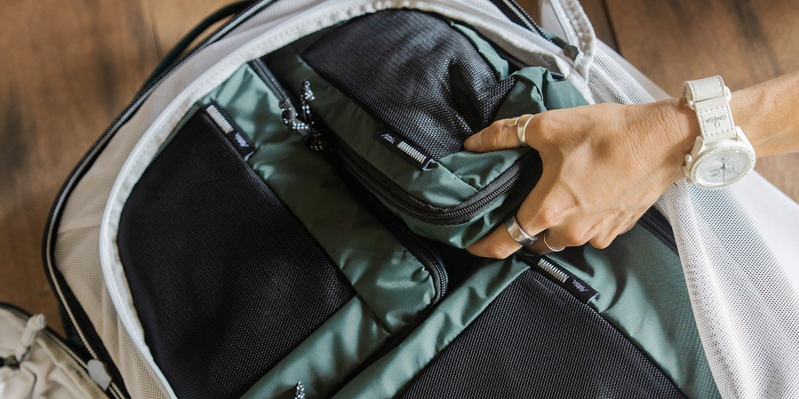 person's handed organizing an open green backpack, showing how to use packing cubes