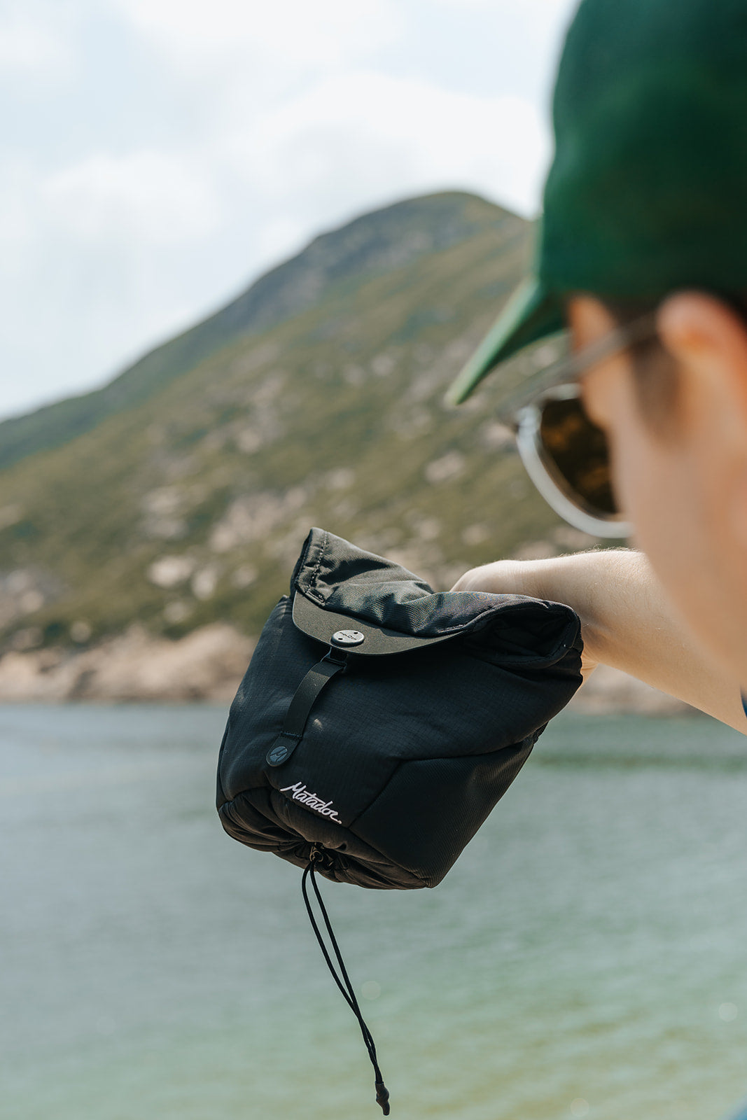 Person holding a black waterproof camera cover case with a scenic background of mountains and water.