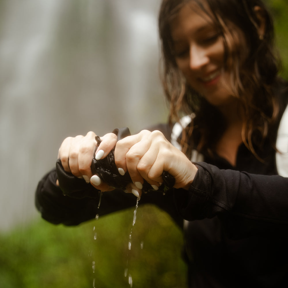 woman in front of waterfall wringing out towel