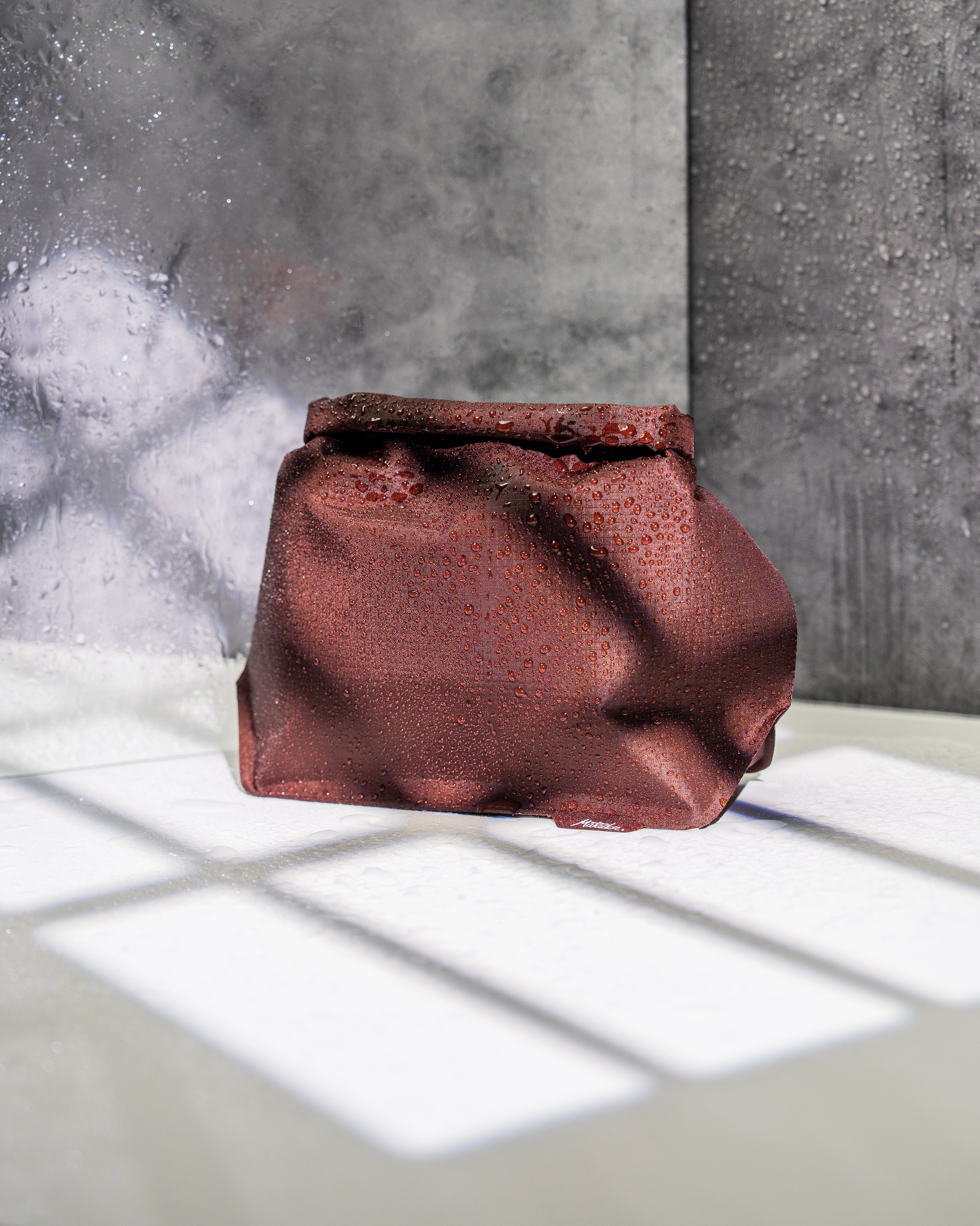 Garnet waterproof travel toiletry case with a roll top closure with a textured gray background