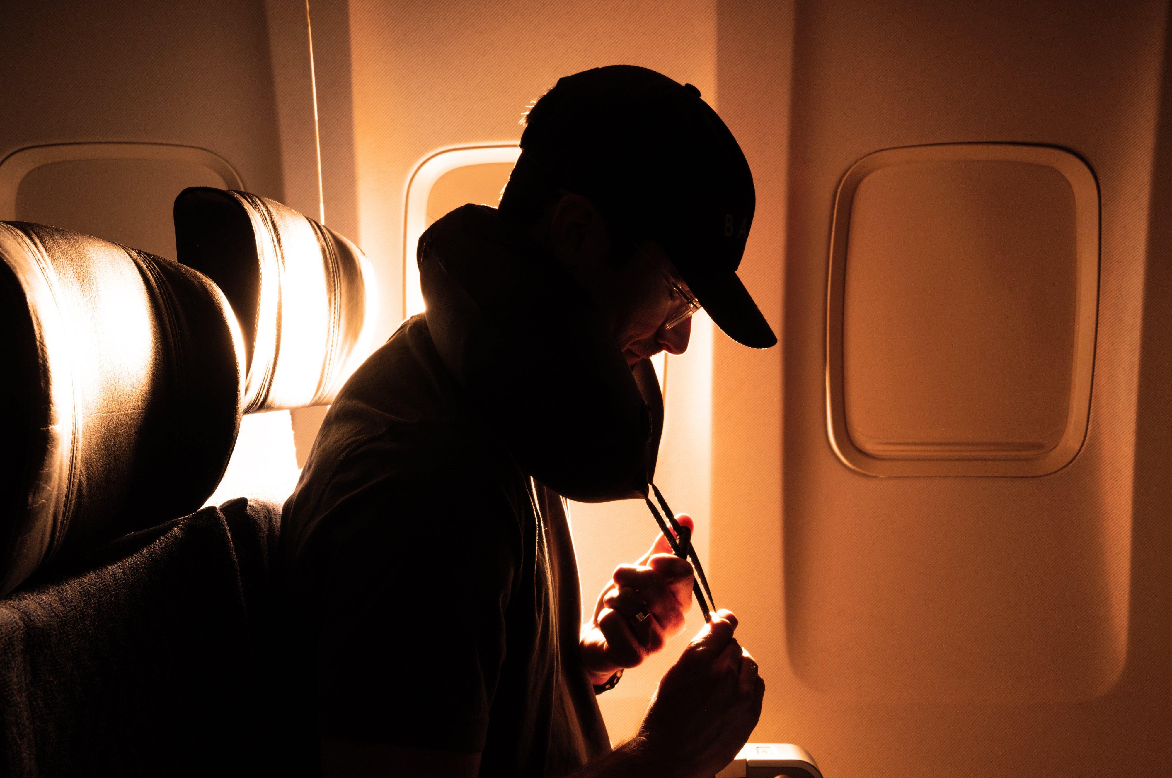 Person sitting in an airplane seat wearing a travel neck pillow, looking out the window.