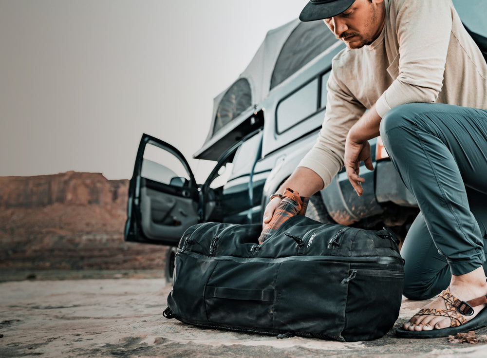 Man in desert, next to camper truck, placing rolled shirt into a pocket of SEG45 travel pack