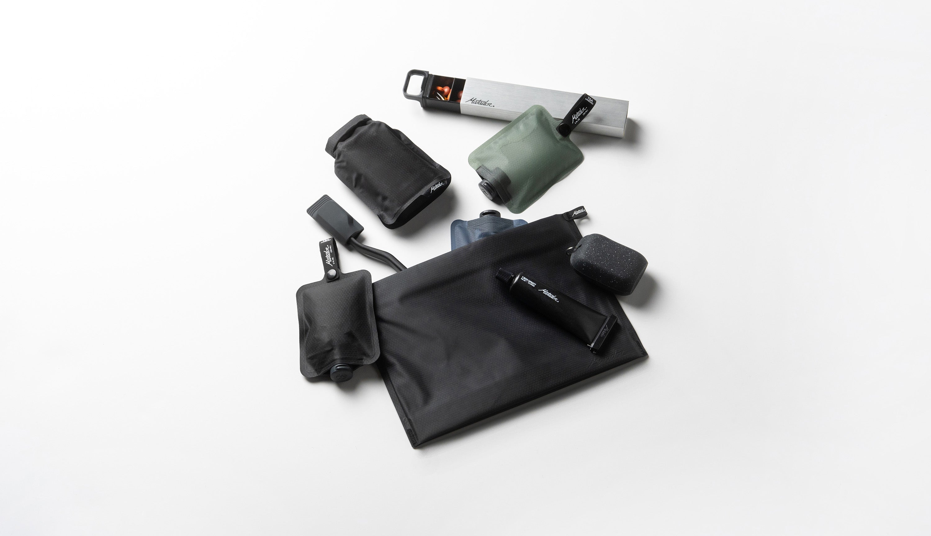 Set of black toiletry cases and silver waterproof pill canister on a white background