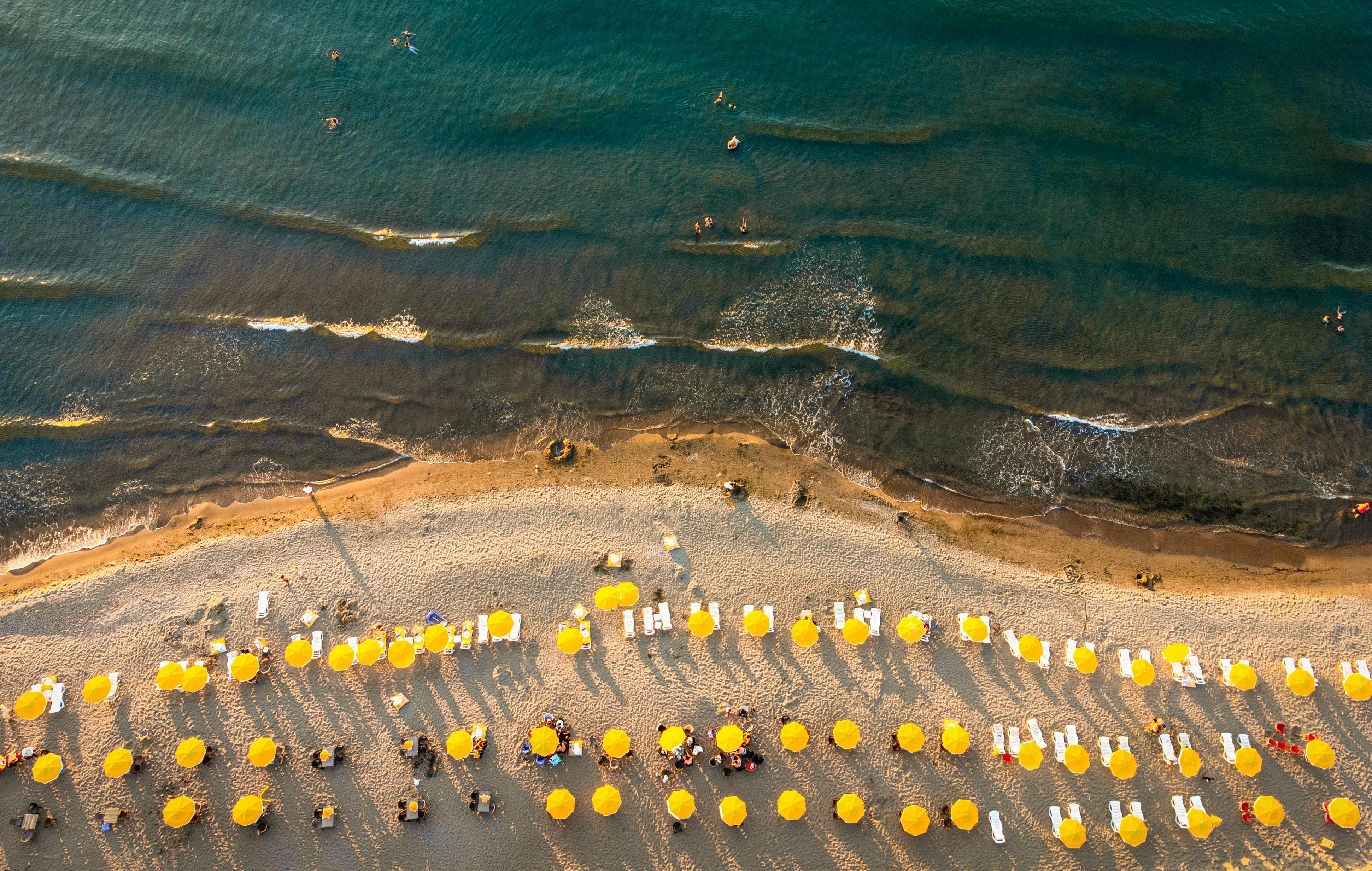 aerial shot of the beach with yellow umbrellas set up for summer travelers