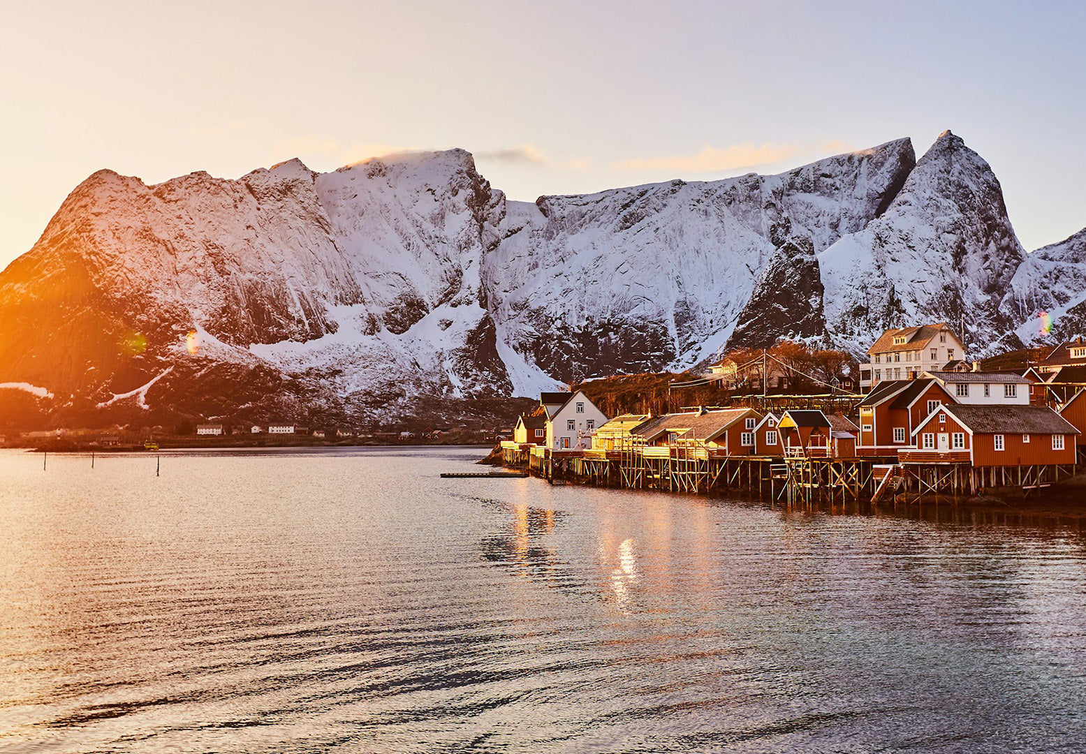 houses in stilts on the water with snow covered mountains behind