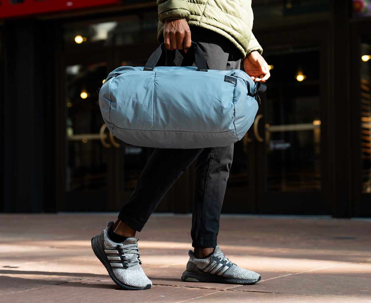 Person holding a light blue duffel bag on a city street