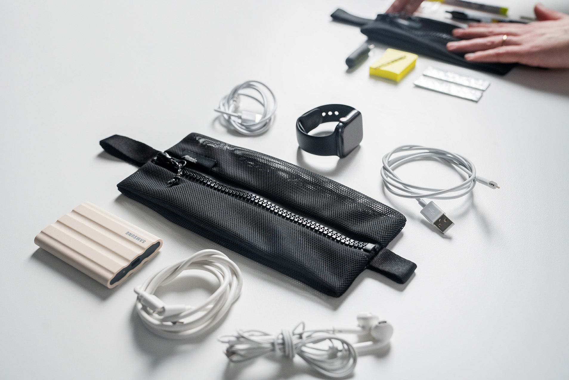 Black mesh organizer pouch with electronic accessories on a white surface