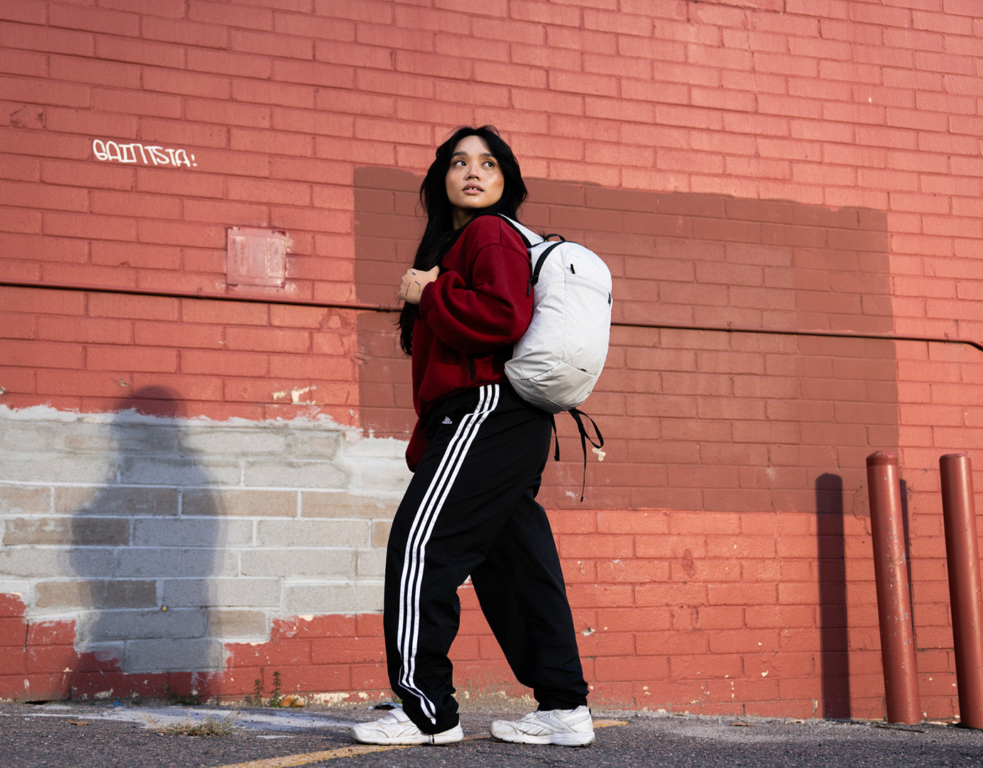Person carrying a white packable backpack against a red brick wall.