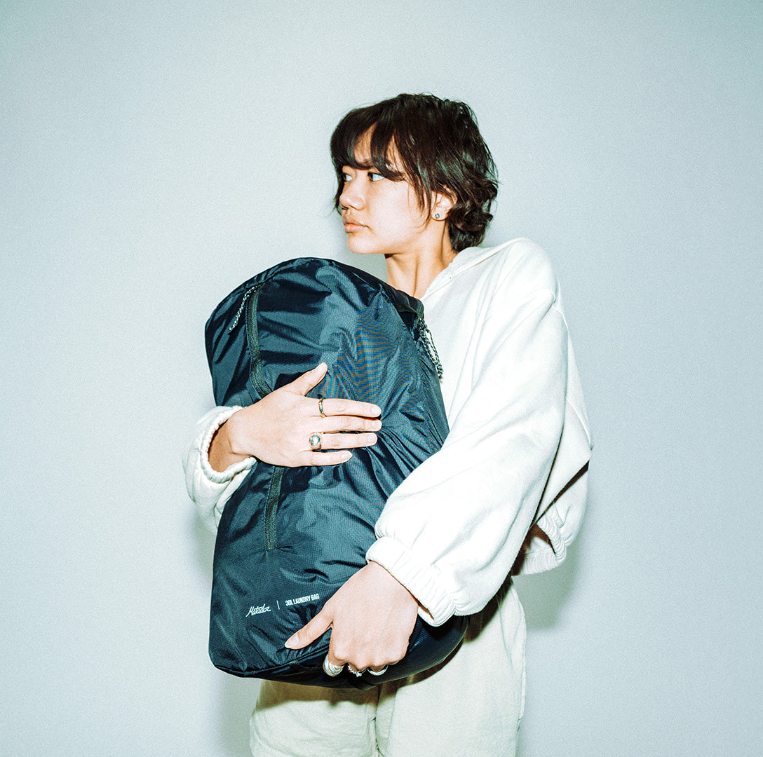 Person holding a black packable laundry bag that's full against a light gray background